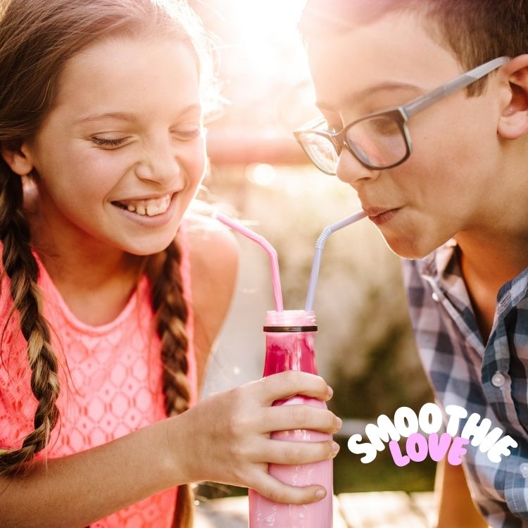 Twee kinderen, een meisje met gevlochten haar en een jongen met een bril, delen een drankje uit een roze fles met behulp van rietjes. Ze lachen en genieten van het moment buiten met zonlicht dat naar binnen stroomt. De tekst "Smoothie Love" staat in de rechteronderhoek, ter ere van de ervaring die mogelijk is gemaakt door de beste smoothieblenders.